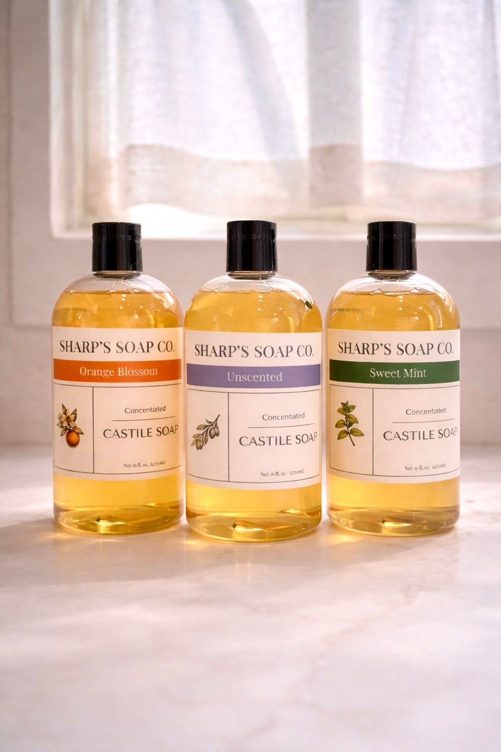Three bottles of Sharp's Soap Oil on a light surface with a white curtain background.