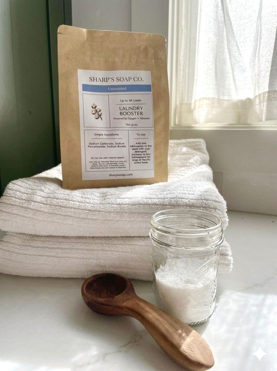 Sharp's Soap Co. laundry booster package on folded towels with a jar of salt and wooden spoon.